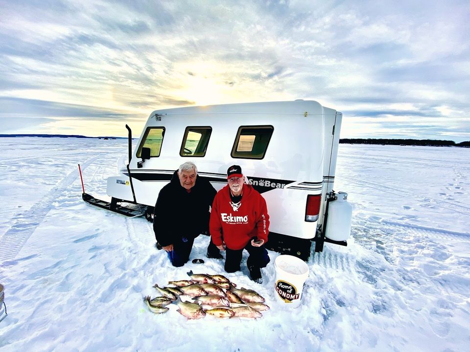 Two anglers kneeling beside a SnoBear on the Devils Lake ice with a day's catch of perch and white bass