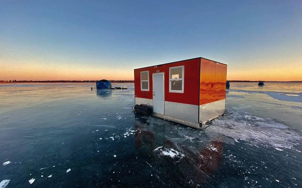 Red Woodland fish house on clear ice at sunset