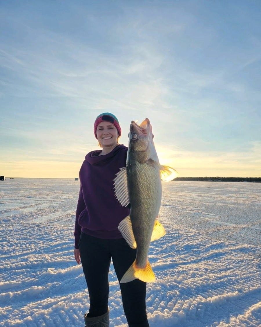 Angler holding a walleye on the ice at sunset